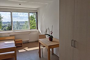 Schülerzimmer des Hufeland-Hauses mit großem Fenster, Bett, Nachttisch, einem weiteren Tisch und einem Kleiderschrank